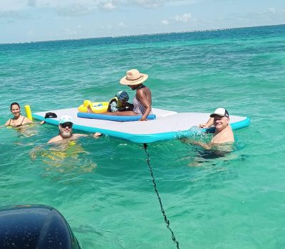 A group of people relaxing on a floating mat in the water near a tiki boat.