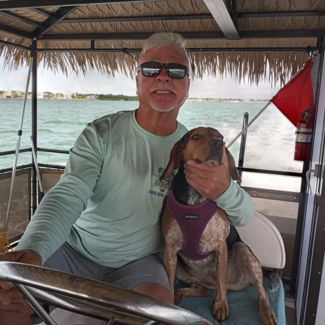A father and daughter smile while enjoying a Key Largo tiki cruise, with the man steering the boat and the ocean in the background.