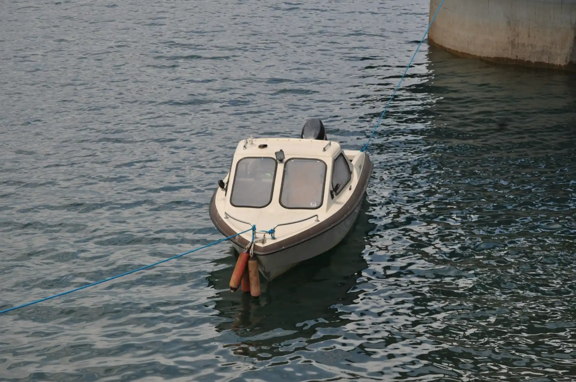 A small, simple motorboat with a cabin floating on calm water, prompting questions like how much are pontoon boat rentals.