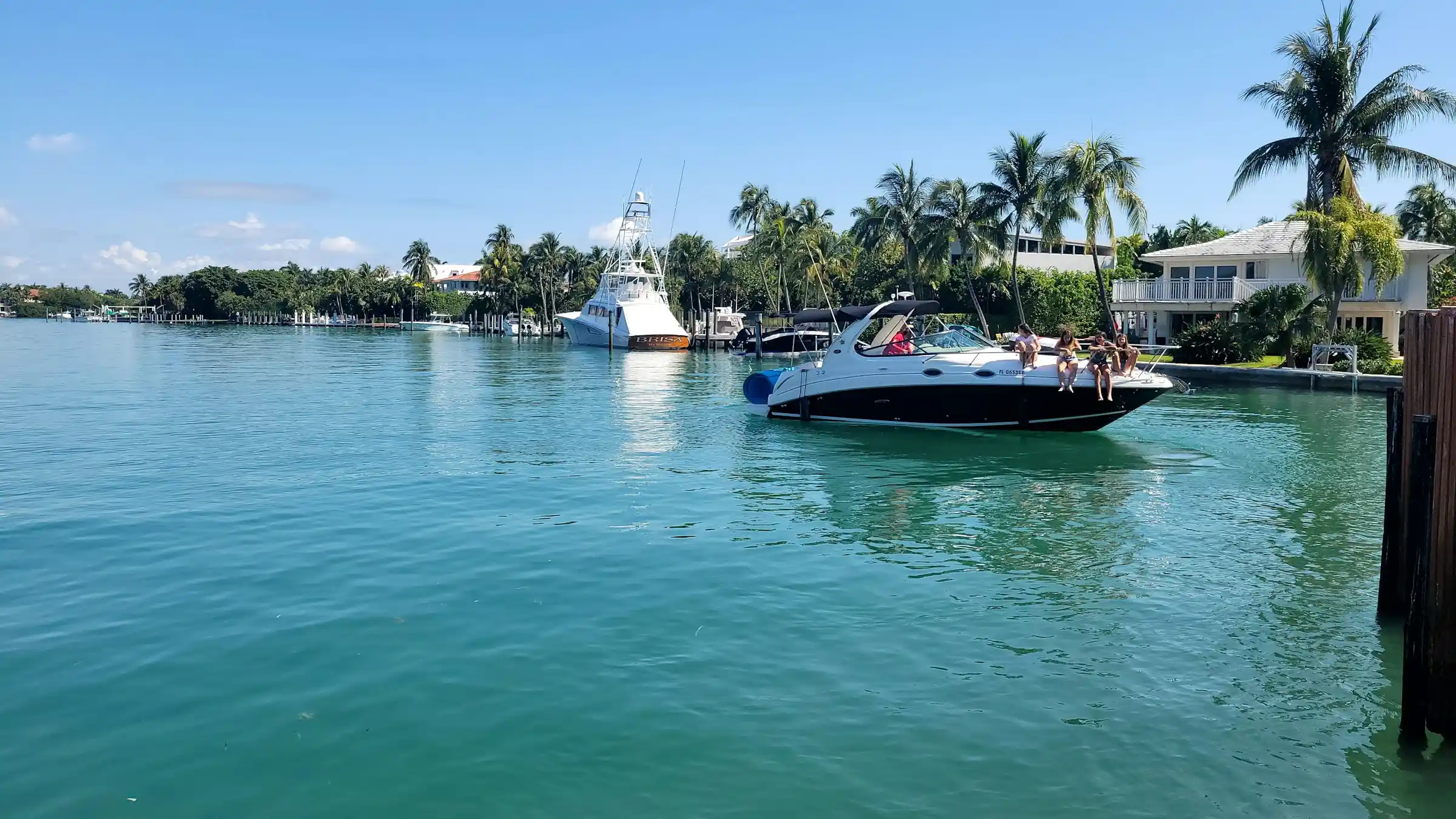 People enjoying themselves on a small motorboat in clear blue water, with houses and palm trees on the distant shore, illustrating the appeal of a rent a boat experience.