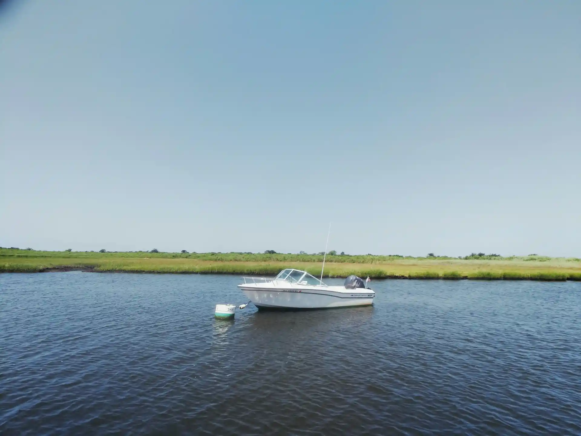 A small white boat anchored in a calm river surrounded by green marshland, hinting at tranquil waters suitable for Boat Rentals With Captain Near Florida.
